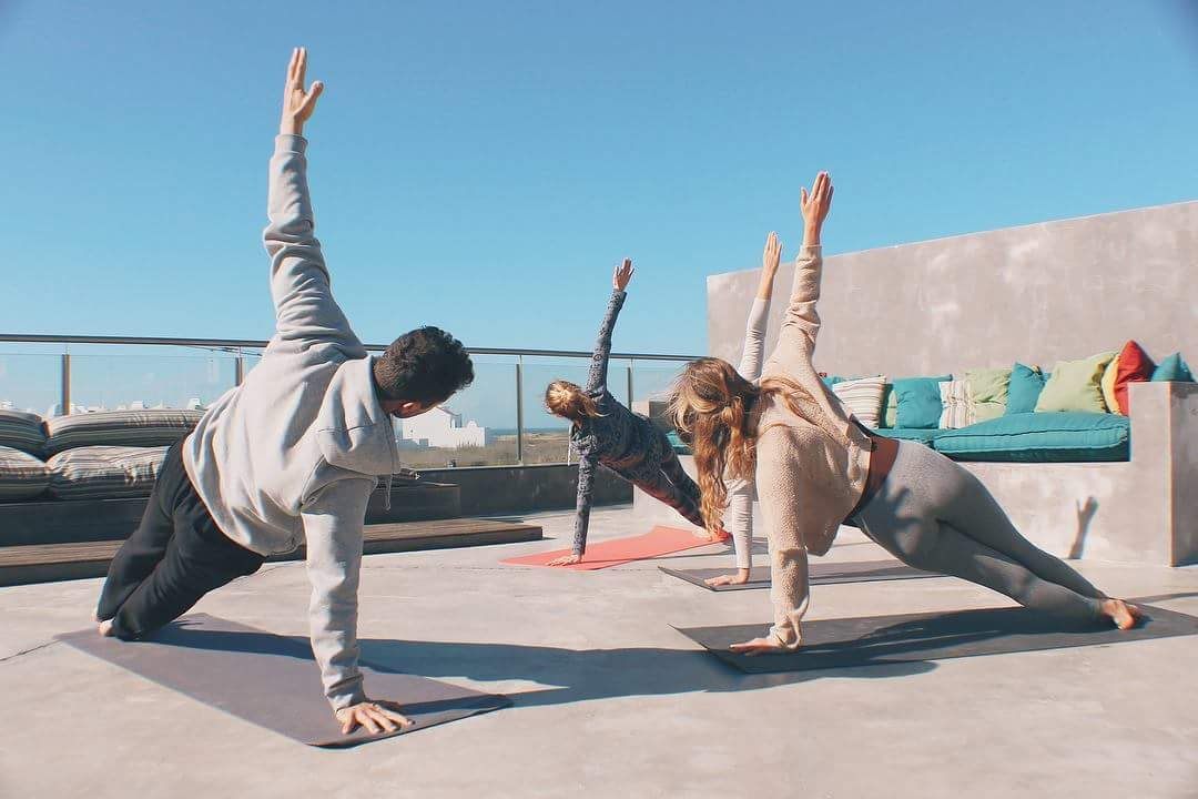 Yoga class on a rooftop terrace by the sea, three people in side plank under a blue sky
