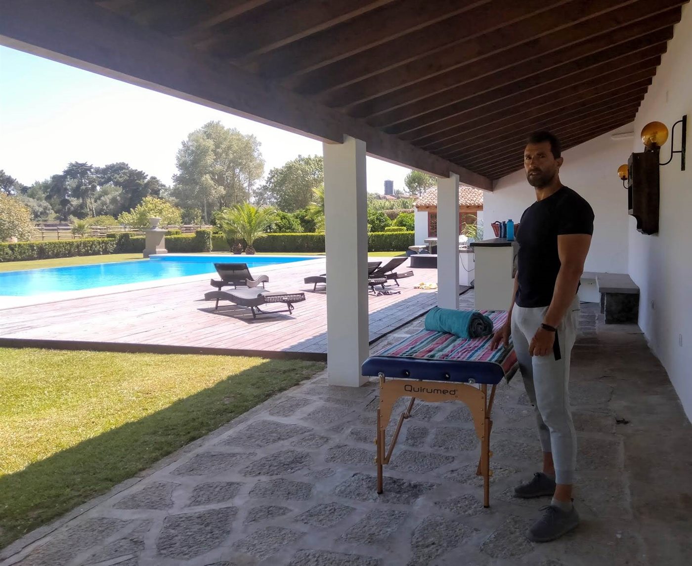 Carlos setting up the massage table on a villa porch, with the pool and garden behind